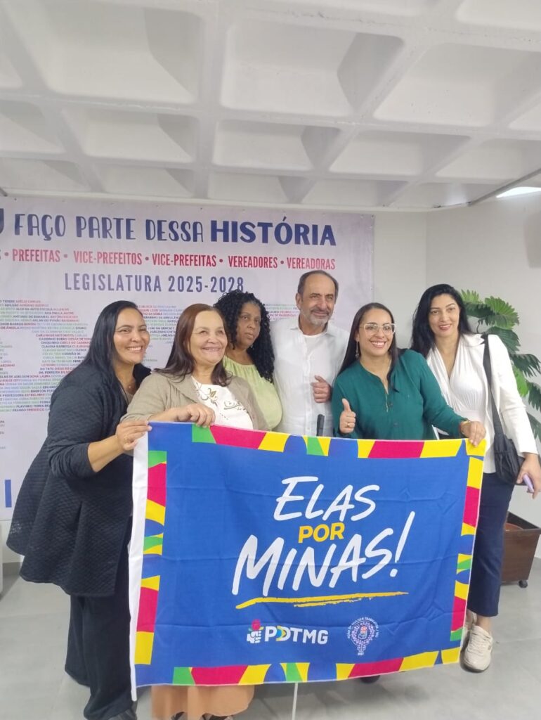 Fotografia de seis pessoas reunidas em um ambiente interno, sorrindo para a câmera e segurando uma grande faixa azul com a mensagem “ELAS POR MINAS!”, acompanhada do logotipo do PDT-MG. Ao fundo, há um painel com a frase “FAÇO PARTE DESSA HISTÓRIA” e referências à Legislatura 2025–2028. O grupo demonstra um momento de união e participação política.