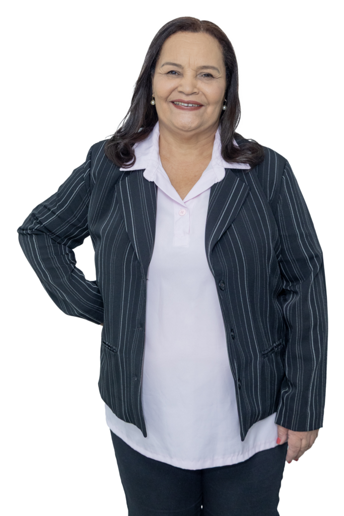 Edna Santos aparece sorrindo, em pé e de frente para a câmera, usando blazer preto com listras finas sobre uma blusa branca. Ela está com uma das mãos apoiada na cintura e a outra ao lado do corpo, em uma pose confiante. A imagem tem fundo transparente.